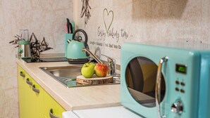 Een keuken met een blauwgroene magnetron, een spoelbak en een houten snijplank met appels.
