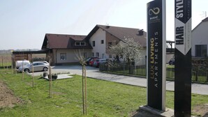 Een woonwijk met een modern appartementencomplex, een parkeerplaats en een bord met 'Budić LUX Living Apartments'.