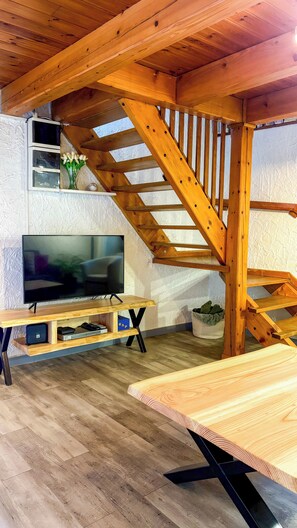 A wooden staircase, a flat-screen TV, and a wooden table in a room with herringbone-patterned flooring. - Villa écrin charance (Gap)