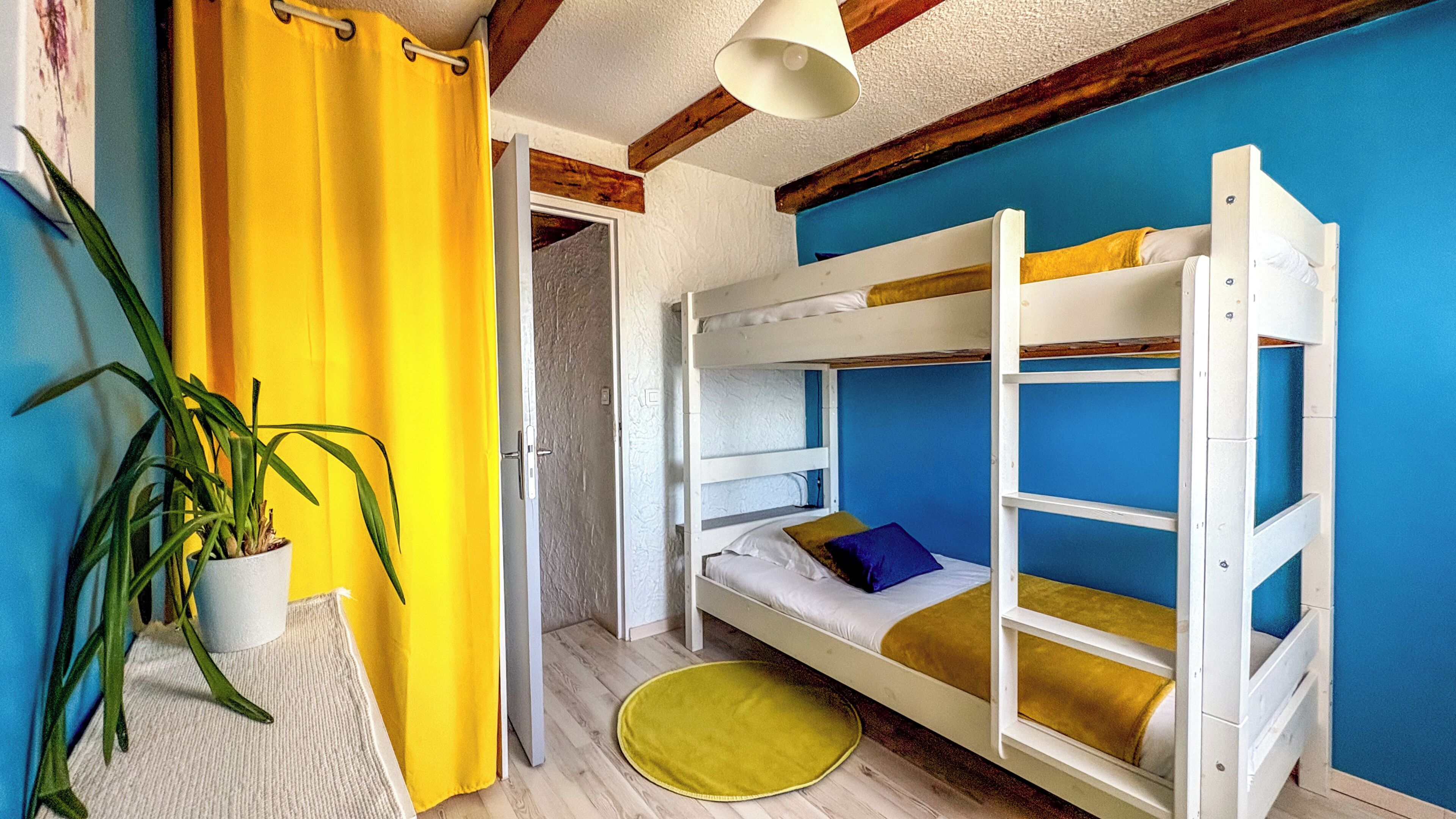 A bunk bed room with a yellow curtain, a potted plant, and a blue wall.