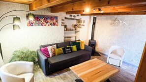 A cozy living room with a sofa, a wooden coffee table, a white chair, a fireplace, and a wall with a textured mural. - Villa écrin charance (Gap)