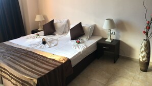 Un lit bien fait, avec du linge de lit blanc et des touches de couleur marron, deux tables de chevet avec des lampes, un vase contenant des fleurs séchées et un couvre-lit à rayures.