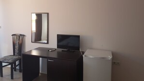 Une pièce de taille modeste comprenant un bureau, une chaise, un téléviseur et un réfrigérateur.