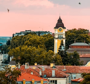 A clock tower with a dome and a balcony, surrounded by trees and buildings with red-tiled roofs. - Salt Lake Aparthotel (Pomorie)