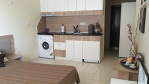 A compact hotel room with a bed, a small kitchenette, a washing machine, and a dining area. - Apart Hotel Salt Lake (Pomorie)