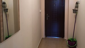 A hallway with a dark door, a mirror, and a mop leaning against the wall. - Apart Hotel Salt Lake (Pomorie)