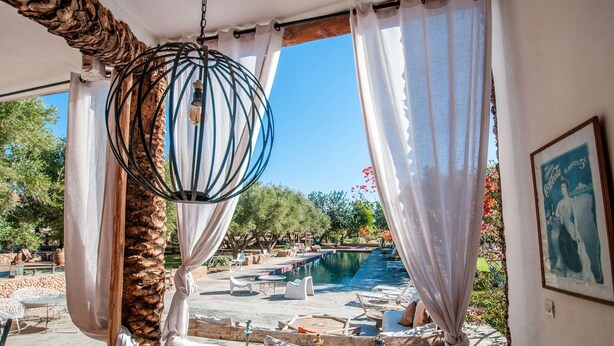 Area piscina con lampadario a sospensione, tende bianche e un quadro appeso al muro.