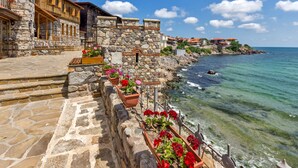 A stone building with a wooden balcony overlooking a clear blue sea. - Flower Street Provides Accommodations With Free Wifi, air Conditioning (Nessebar)