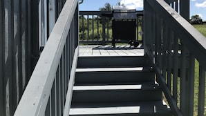 A wooden staircase leading to a deck with a barbecue grill.