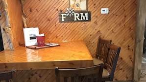 A wooden dining table with four chairs, a framed picture of a cow, and a thermostat on the wall.