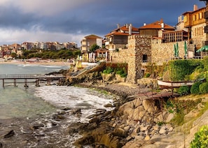 A coastal hotel with stone architecture, a rocky shoreline, and a pier extending into the sea.