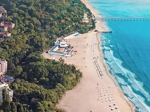 Vue aérienne d’une zone côtière comprenant une plage, une jetée et un ensemble de bâtiments comprenant plusieurs structures.