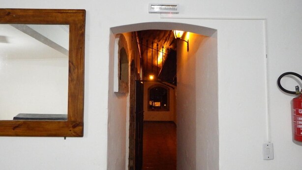 A narrow hallway with a wooden-framed mirror on the left, a fire extinguisher on the right, and a sign above the door. - O Hostel GRU-SP (Guarulhos)