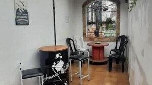 A patio area with tiled flooring, a drum set, and a drum stool. There is a window with a view of a tall building. - O Hostel GRU-SP (Guarulhos)