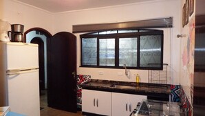 A compact kitchen with a refrigerator, a stove, and a window with blinds. - O Hostel GRU-SP (Guarulhos)