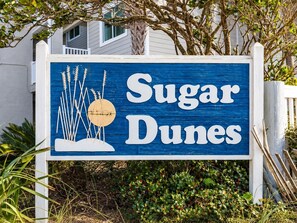A sign with the text 'Sugar Dunes' and decorative elements including wheat stalks and a circular object.