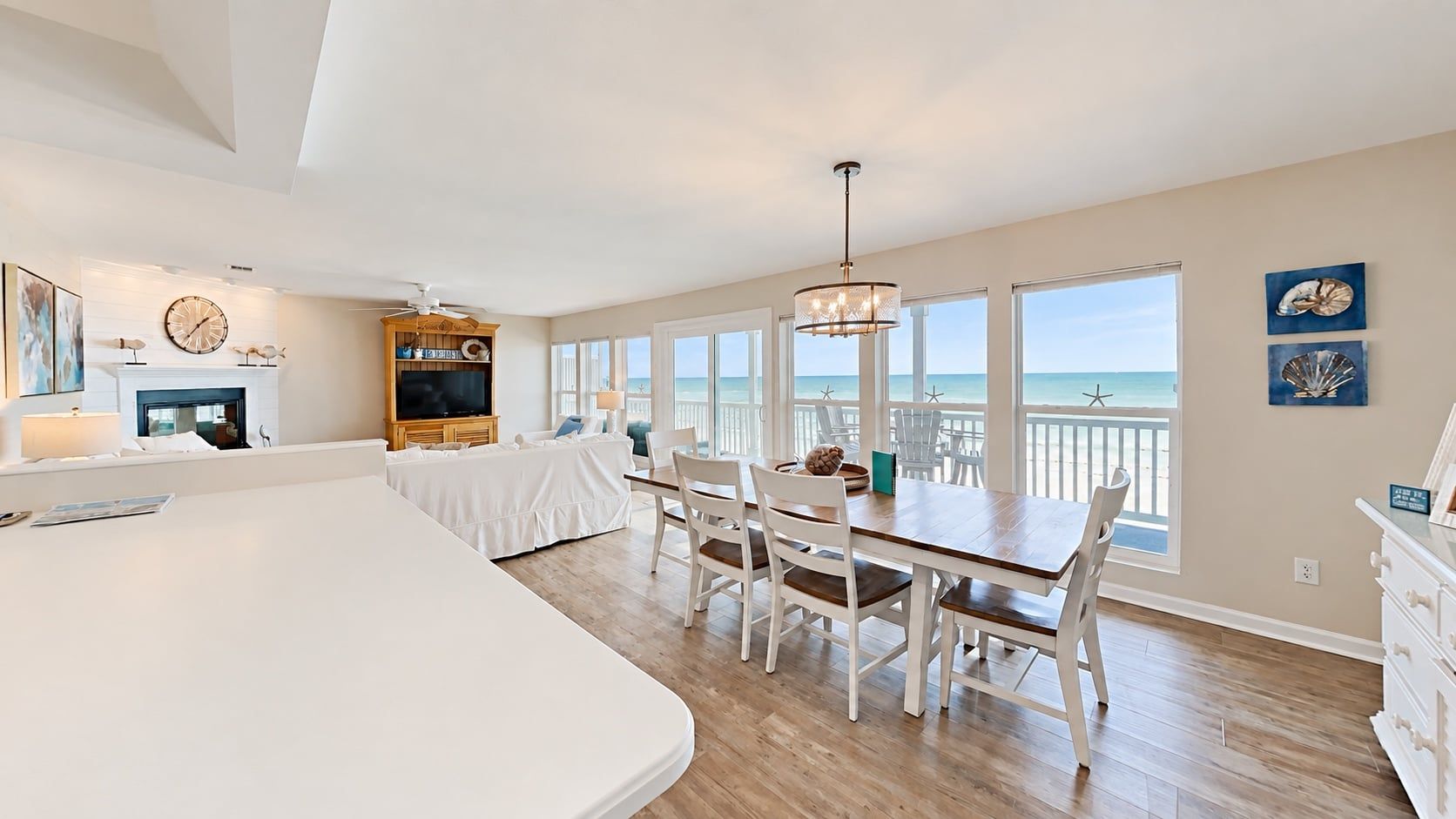 A spacious room with a large dining table, white furniture, a TV, and a view of the ocean.