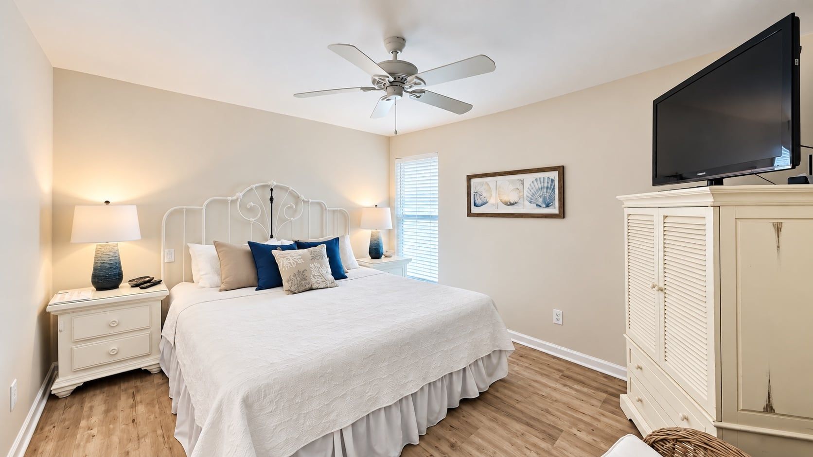 A bedroom with a bed, nightstands, a ceiling fan, a television, and a cabinet.