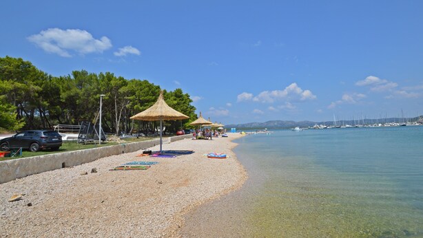 A beach with clear water, umbrellas, and boats.
