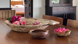 Un comedor con una mesa rústica, un cuenco grande con flores, un cuenco más pequeño y una silla de mimbre.