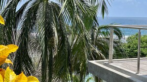 Un balcón con vista al océano, rodeado de palmeras y vegetación.
