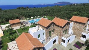 A resort with stone buildings, a swimming pool, and a view of the sea.