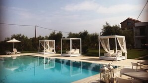 En swimmingpool med solstolar och parasoller, omgiven av grönska och ett hus.