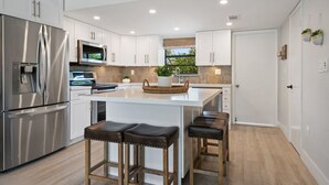 A modern kitchen with a stainless steel refrigerator, a microwave, and a large island with bar stools. - Key Largo Villa, Kawama J3, 3/3, Ocean,Marina,Lagoon,Pools,Kayaks&bikes (Key Largo)