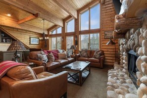A log cabin interior with leather sofas, a coffee table, and a stone fireplace.
