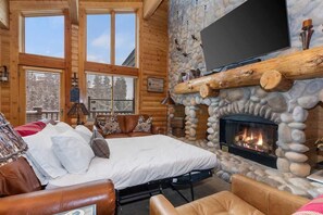 A log cabin interior with a bed, fireplace, and large windows.