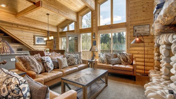 A log cabin interior with a wooden ceiling, large windows, a fireplace, and a stone wall. - Abode at Black Bear #403, hot tub, pool & gym, steps to trails (Park City)