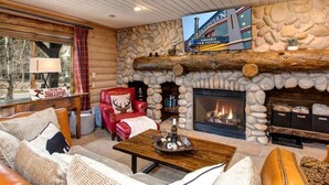 A log cabin interior with a stone fireplace, a red leather chair, a wooden coffee table, and a television mounted on the wall. - Abode at Black Bear #103, hot tub, pool & gym, Deer Valley (Park City)
