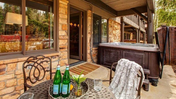 An outdoor patio with stone walls, a hot tub, and a table with bottles and glasses. - Abode at Black Bear #103, hot tub, pool & gym, Deer Valley (Park City)