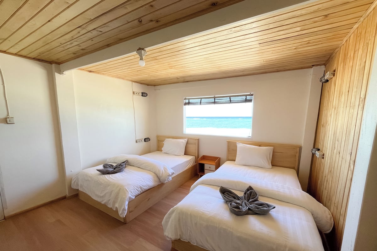Una habitación con dos camas, una ventana que da al mar y vigas de madera en el techo.