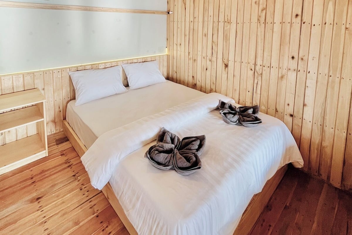 Una habitación de madera con una cama, una mesita de noche y un panel de pared de madera.