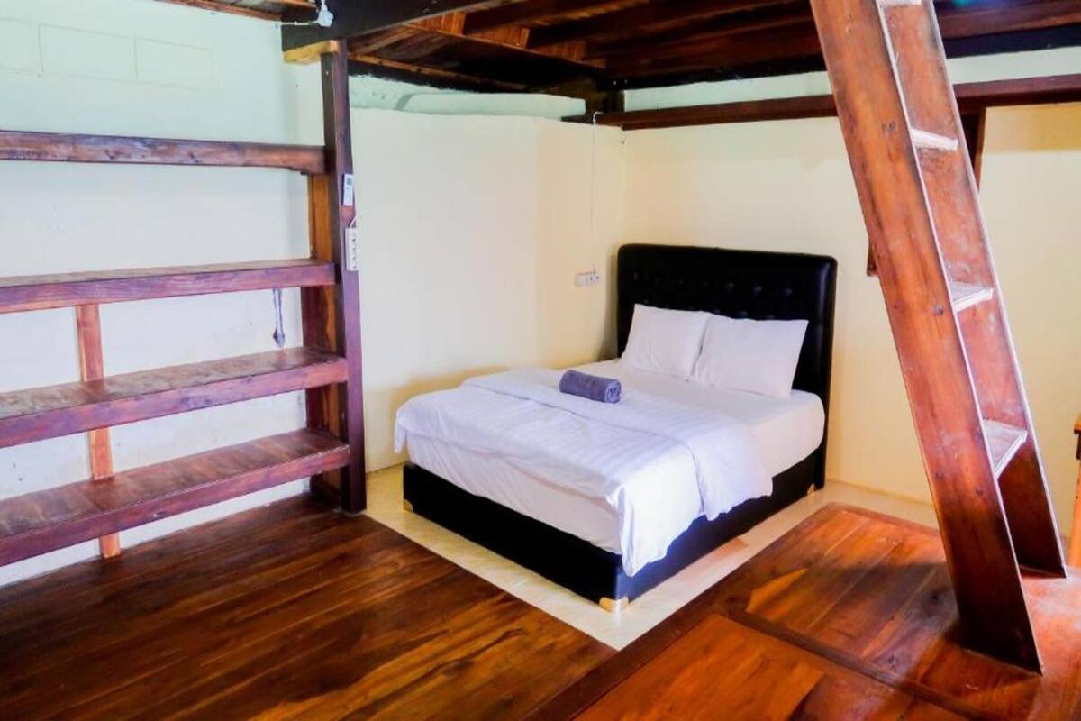 Un dormitorio con estructura de cama de madera, ropa de cama blanca y una escalera de madera apoyada en la pared.