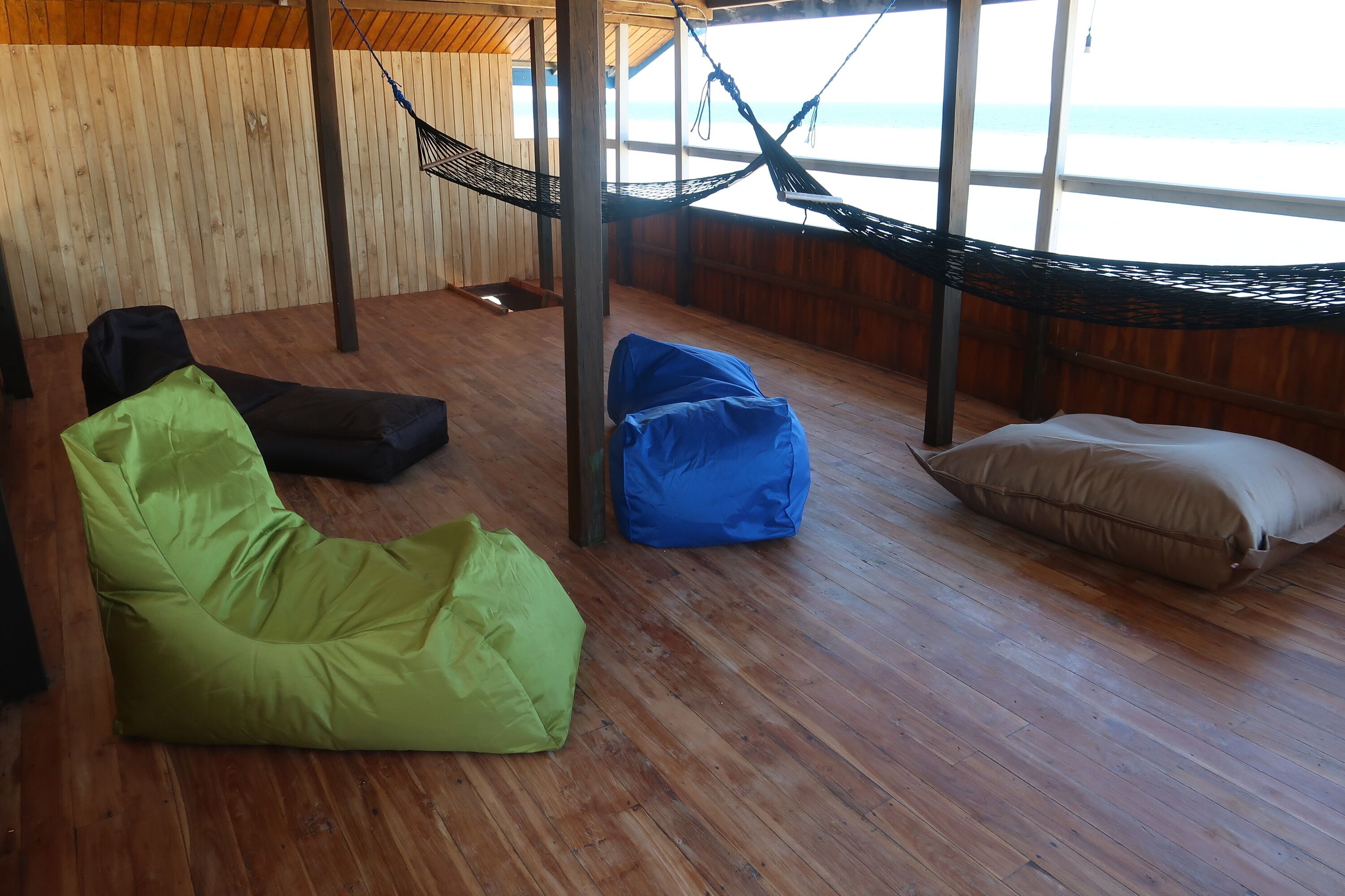 Een kamer met een hangmat, groene en blauwe krukkonen en een bruin kussen.