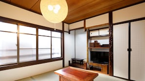 Ein traditioneller japanischer Raum mit Tatami-Bodenbelag, einem Holztisch, Schiebetüren und einem Fernseher.
