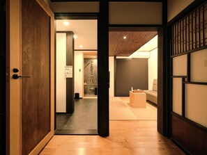 A traditional Japanese interior with a wooden door, a tatami mat floor, a sliding shoji screen, and a modern shower area.