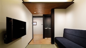 Ein Flur mit an der Wand montiertem Flachbildfernseher, einem dunklen Sofa und Holzboden.
