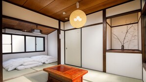 Ein traditioneller japanischer Raum mit Tatami-Böden, einem niedrigen Holztisch, Schiebetüren und einer hängenden Leuchte.