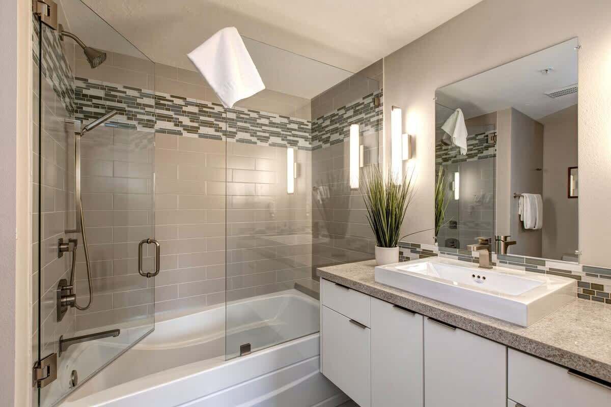 Un baño moderno con ducha envuelta en vidrio, una bañera independiente y un espejo grande sobre el lavamanos.