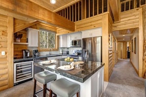 A log cabin-style kitchen with a central island, stainless steel appliances, and wooden walls.