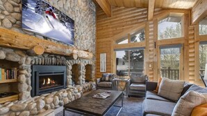 A log cabin interior with a stone fireplace, a television mounted on the wall, and a cozy seating area with a sofa and armchairs. - Abode at Black Bear #431, hot tub, pool, free Main Streetreet shuttle (Park City)