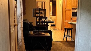 Un pasillo que conduce a una sala de estar con un sofá, una mesa de centro y una alfombra. Se ve una escalera que sube a otro nivel.