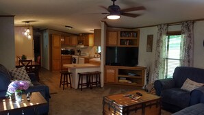 Una sala de estar con un sofá, una mesa de centro y un televisor. Cuenta con una zona de cocina con armarios de madera y un microondas.