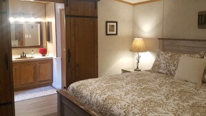 Un dormitorio con cama, mesita de noche, lámpara, cómoda, espejo y puerta.