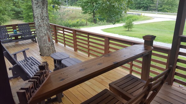 Eine Holzterrasse mit Bänken und Tischen, mit Blick auf eine Rasenfläche und eine Straße.