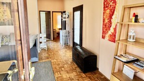 A hotel room with a wooden parquet floor, a bed with a grey headboard, a small wooden chest, and a shelf with books and a white lantern. - Sunny island (Stari Grad)