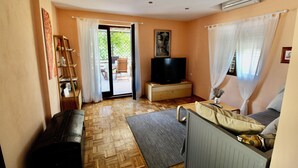 A living room with a sofa, a television, a wooden floor, and a sliding glass door leading to an outdoor area. - Sunny island (Stari Grad)